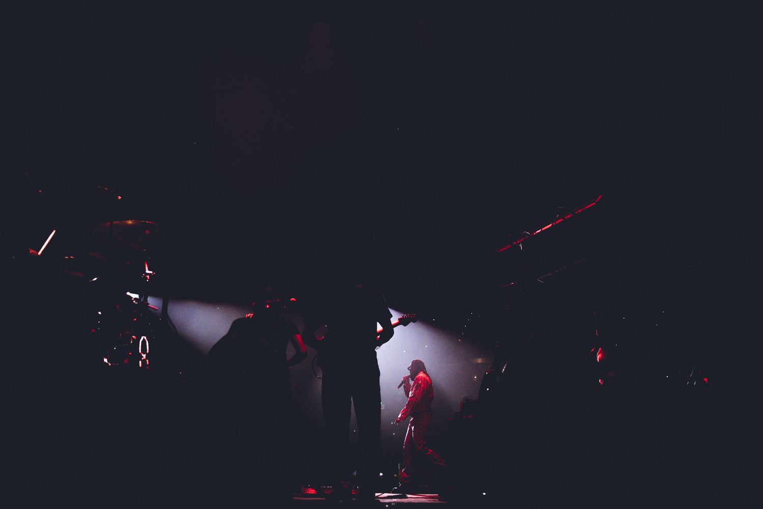 Stage performer silhouetted against twin white spotlights during dark concert performance.
