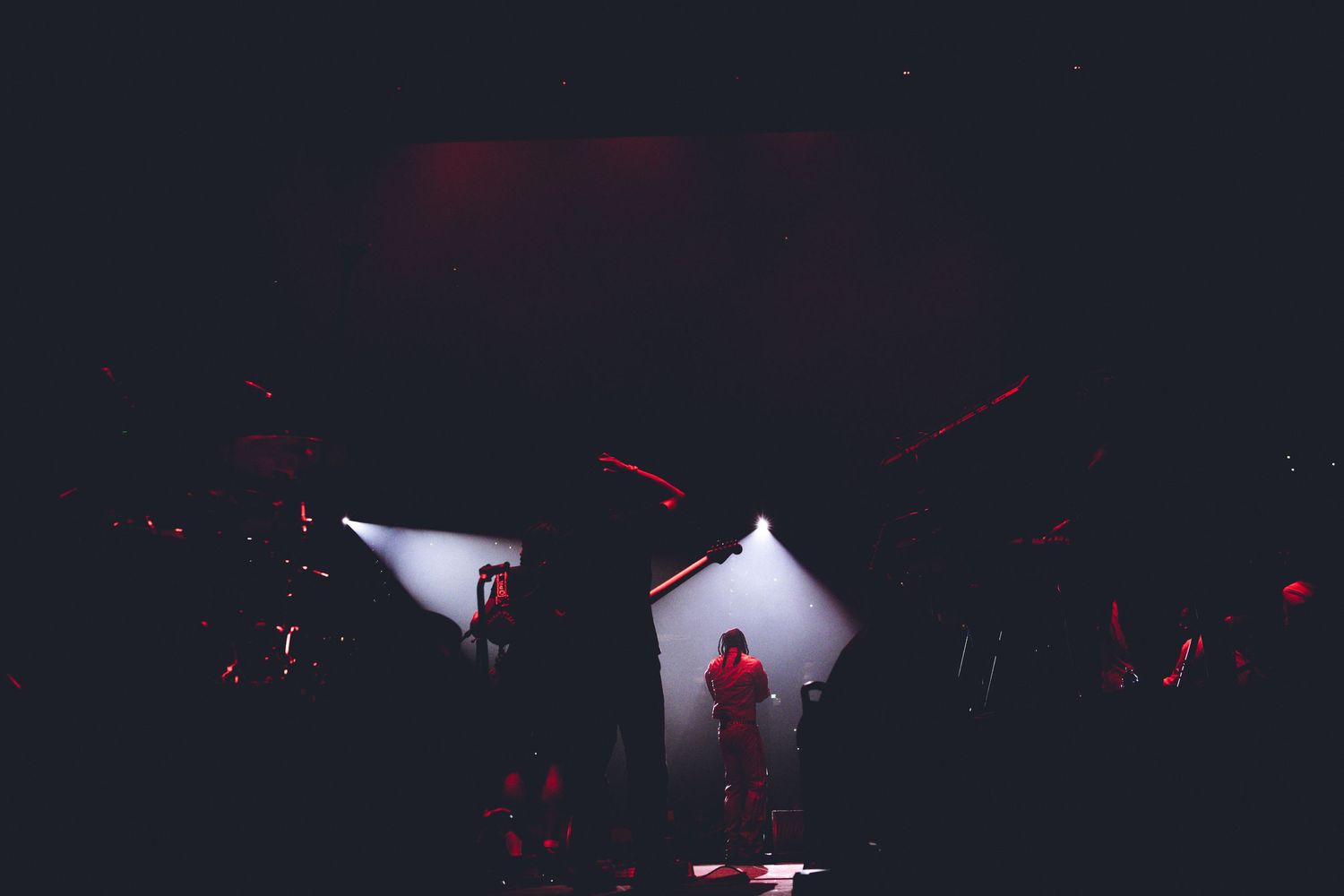 Dramatic silhouette of performer on stage framed by white spotlights in dark venue.