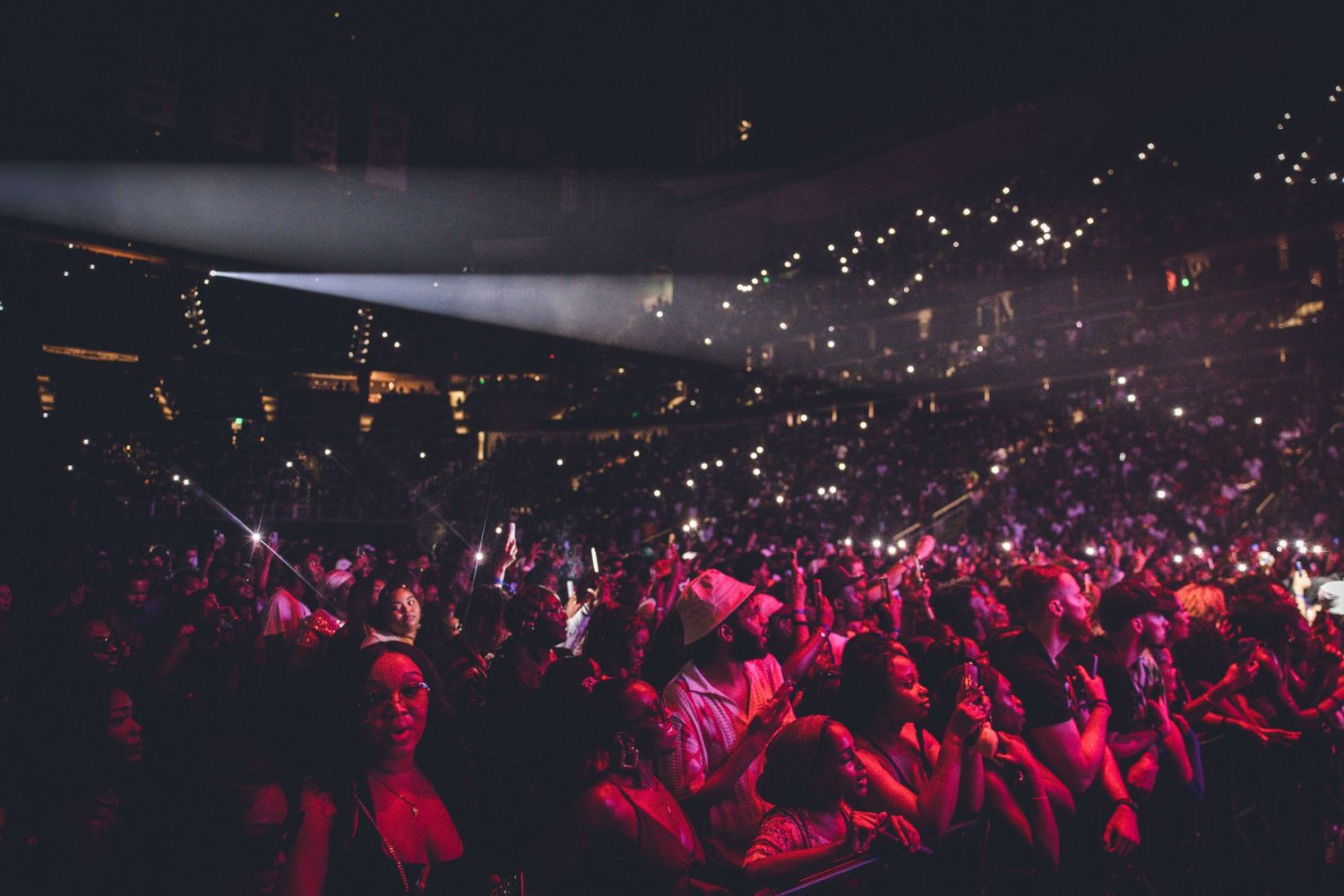 Concert crowd illuminated by spotlight beams with phone lights creating starry effect.
