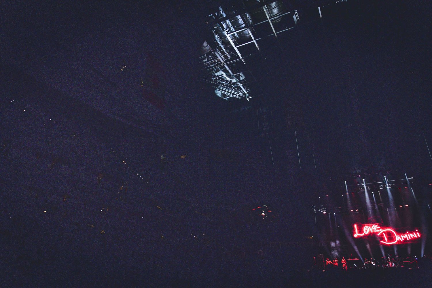 Dark concert venue with stage rigging and red neon signage visible against night sky.