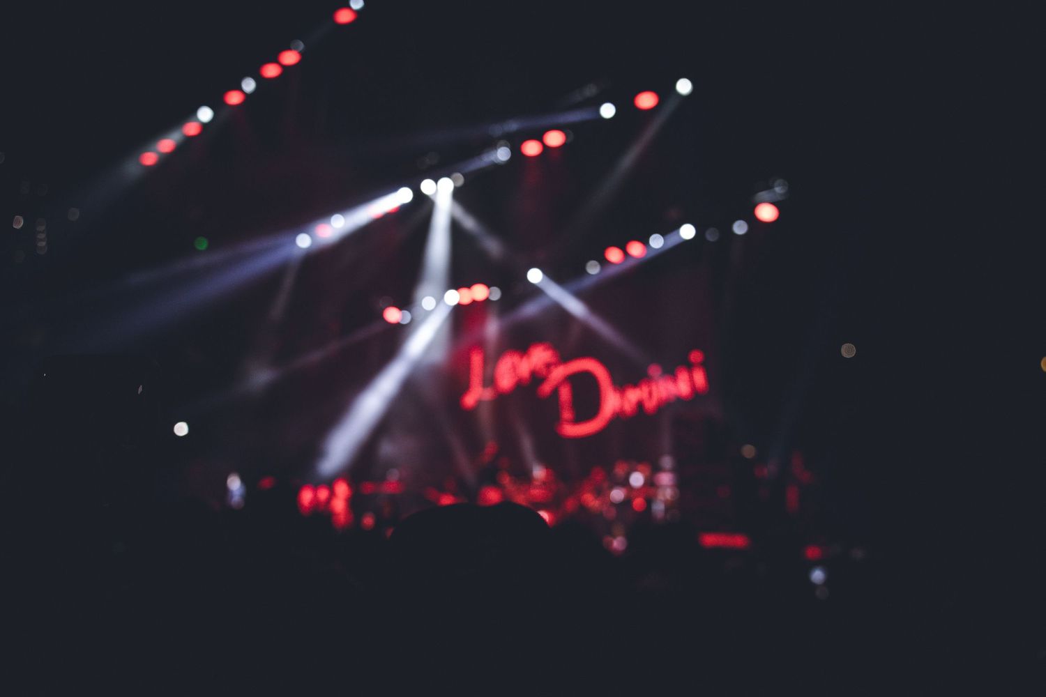 Blurred concert lighting and neon sign with dramatic spotlights cutting through darkness.