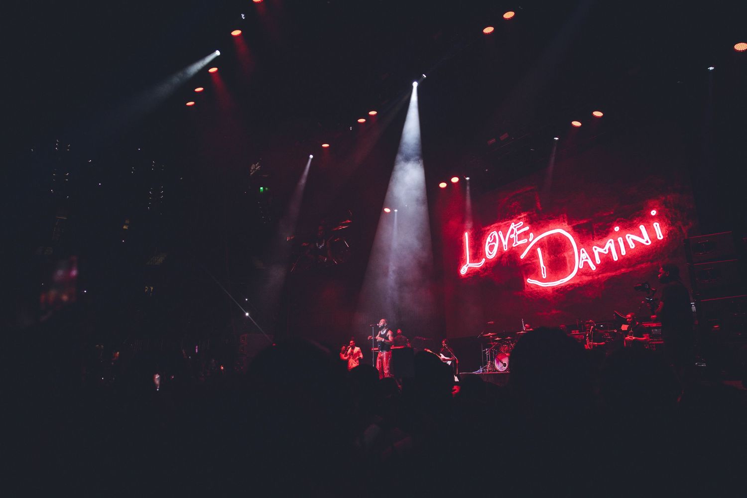 Red neon sign glowing in dark concert venue with spotlights illuminating the stage.