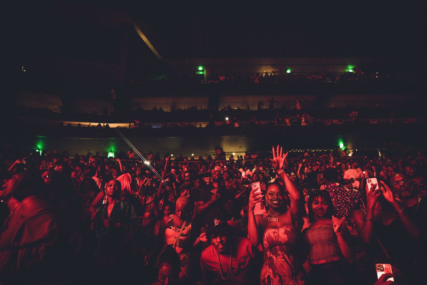 Energetic concert crowd with raised hands silhouetted against red stage lighting.