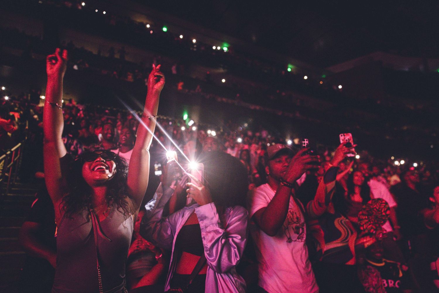 Music fans dancing and cheering at a concert venue bathed in dramatic red lighting.