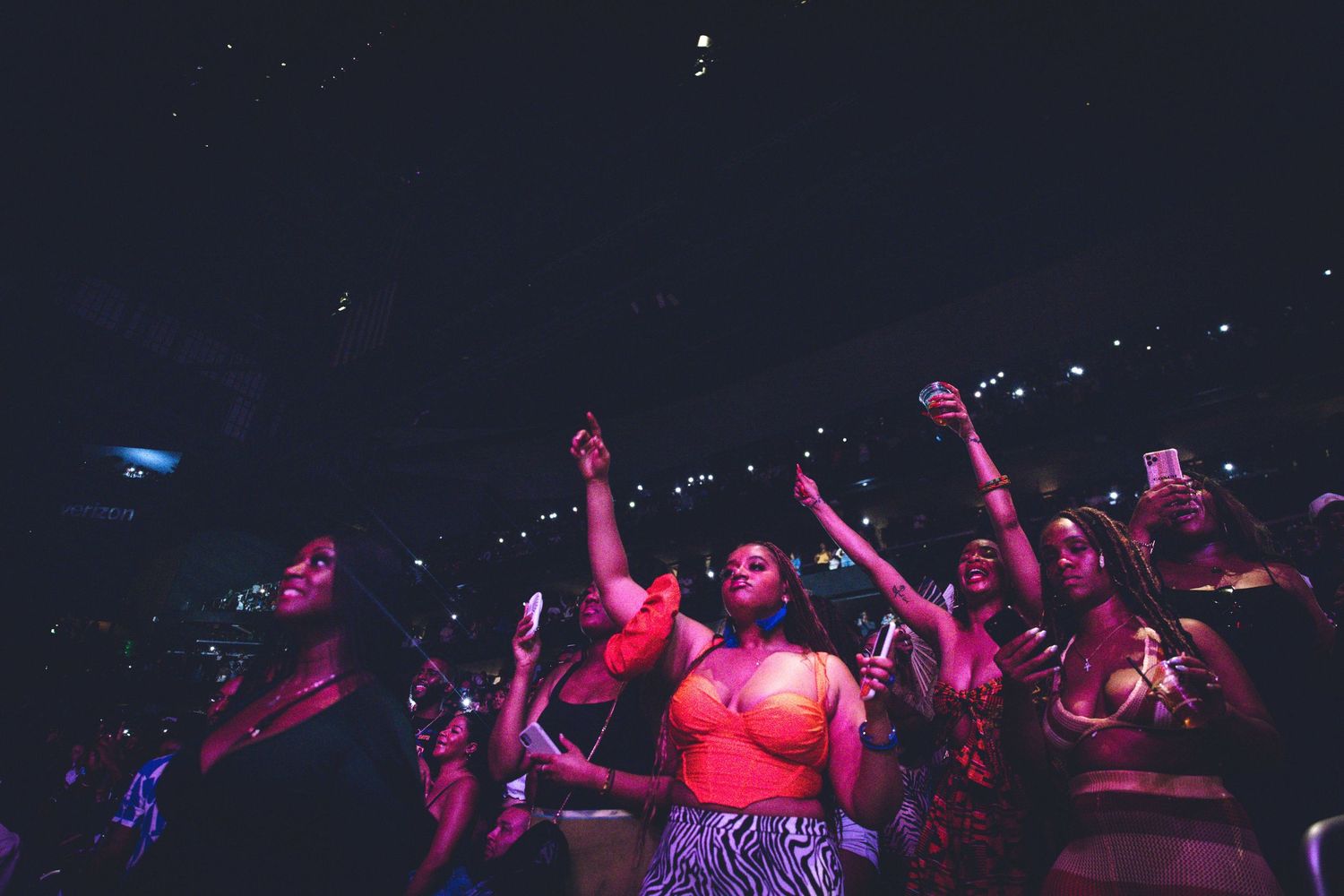 Concert crowd bathed in pink and purple lighting with raised hands enjoying the performance.