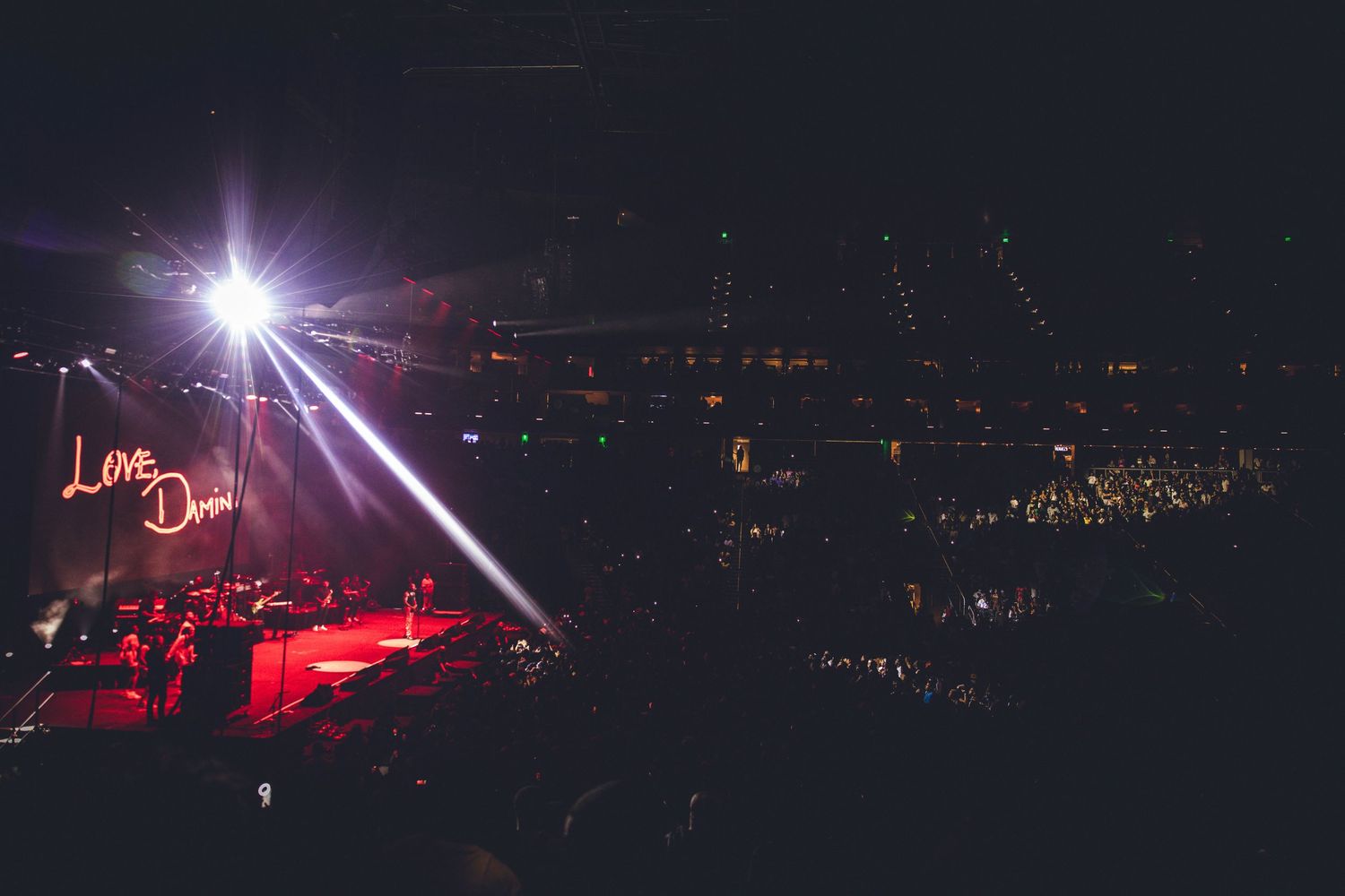Bright stage lights illuminate a concert venue with red lighting effects creating an atmospheric scene.