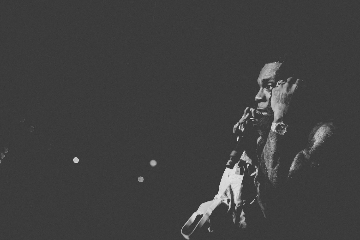 A dramatic black and white shot of a performer singing into a microphone on a dimly lit stage.