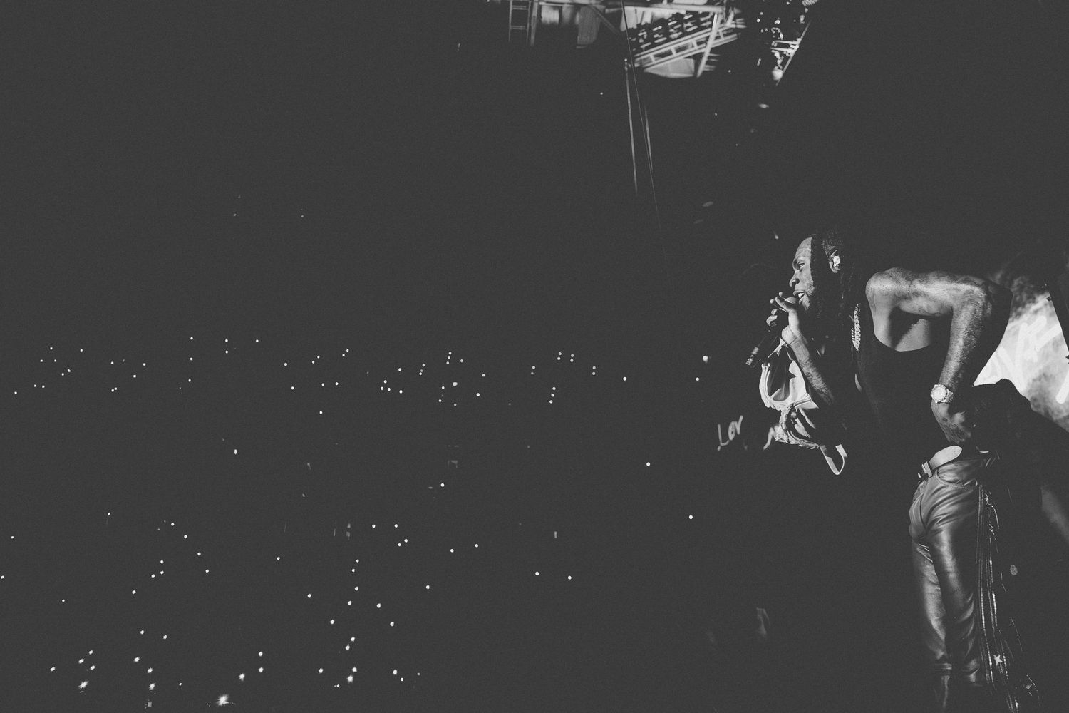 A concert performer silhouetted against bright stage lights while entertaining a large crowd.