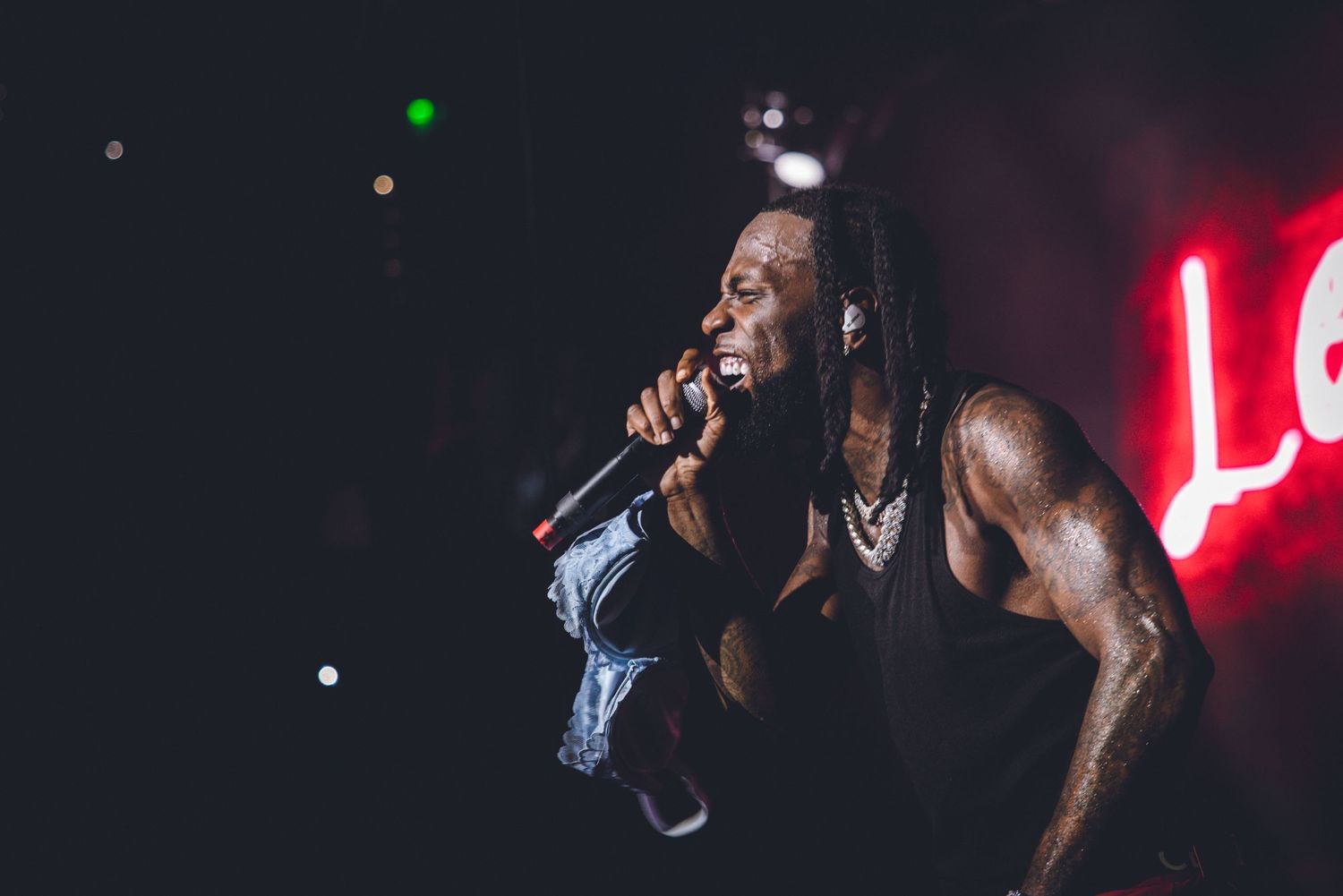 A performer sings passionately on stage with dramatic red lighting and dark atmosphere during a concert performance.