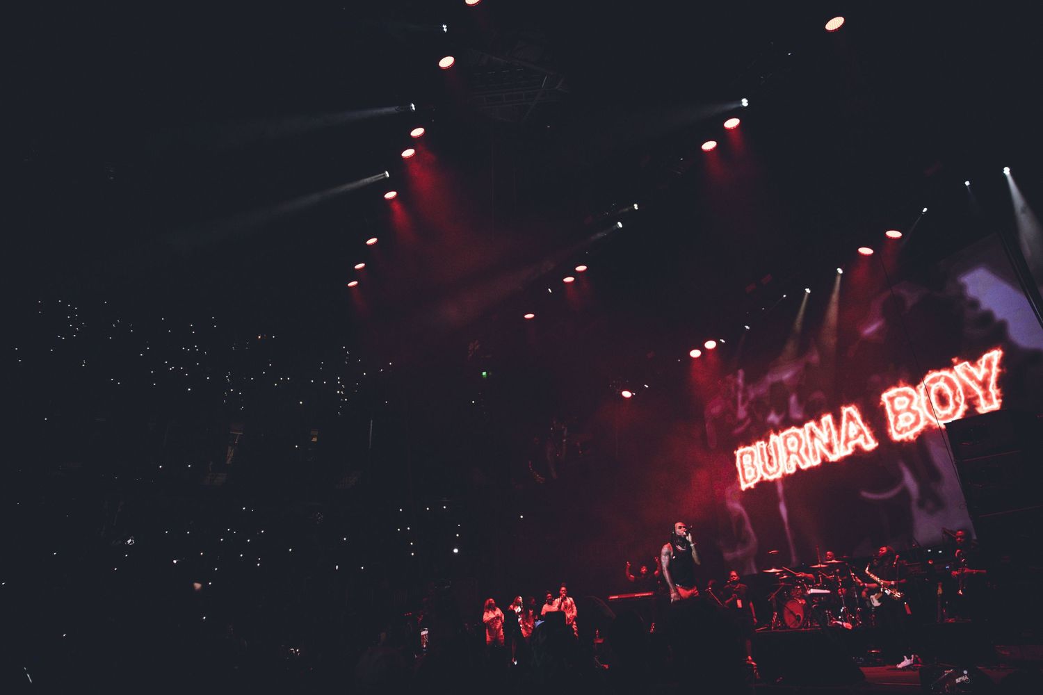 Neon 'BURNA BOY' sign glows in red against dark concert venue backdrop.