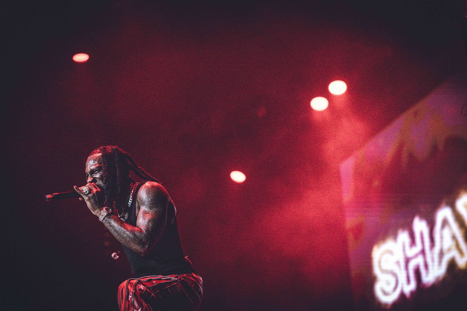 Concert performance captured in red stage lighting with 'SHA' text visible.