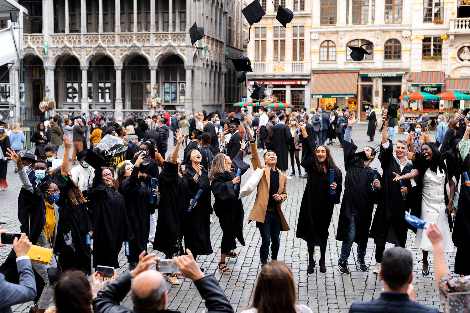 Graduates celebrate by throwing their mortarboard caps in the air outside a historic building in Grand Place, Brussels.