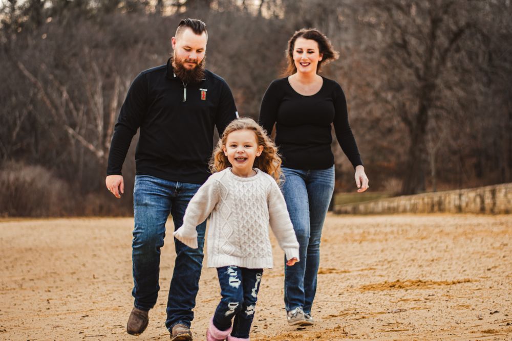 Family running together on a dirt path during autumn with natural scenery in background.