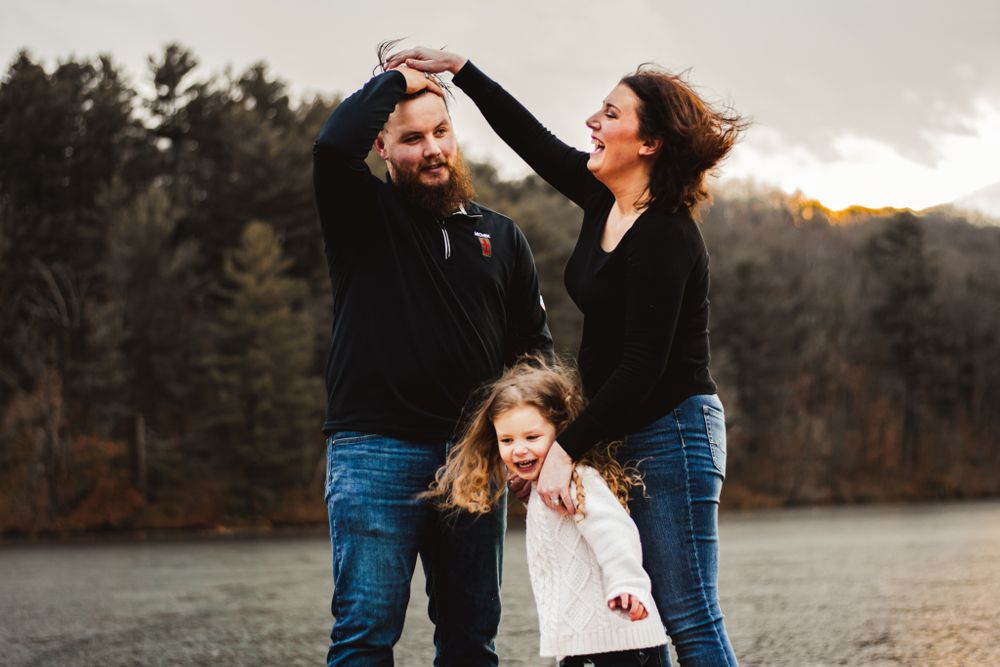 A family shares a playful moment together on a wooden dock at sunset.