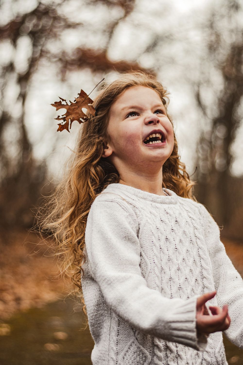 Pure joy radiates through laughter as autumn leaves flutter in a wooded setting.