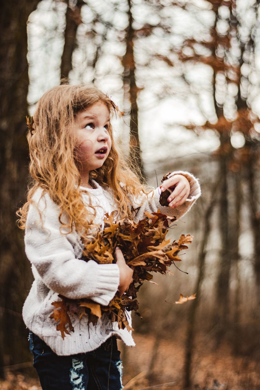 A cozy sweater-wearing child gathers fallen leaves during an autumn day in the woods.