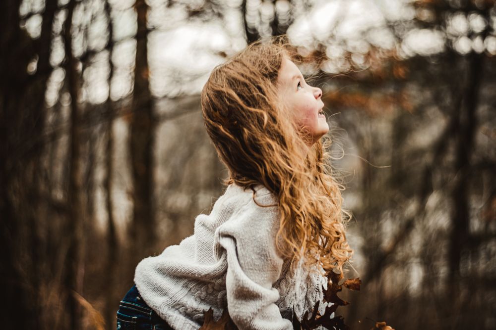 Wavy hair flows in the wind against a moody forest backdrop during fall.
