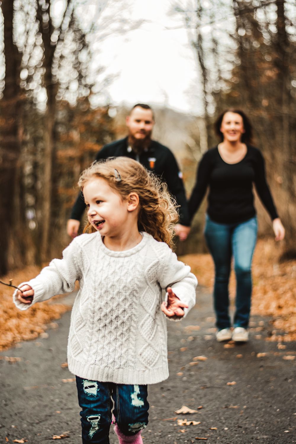 A child runs joyfully down a forest path while adults follow behind.