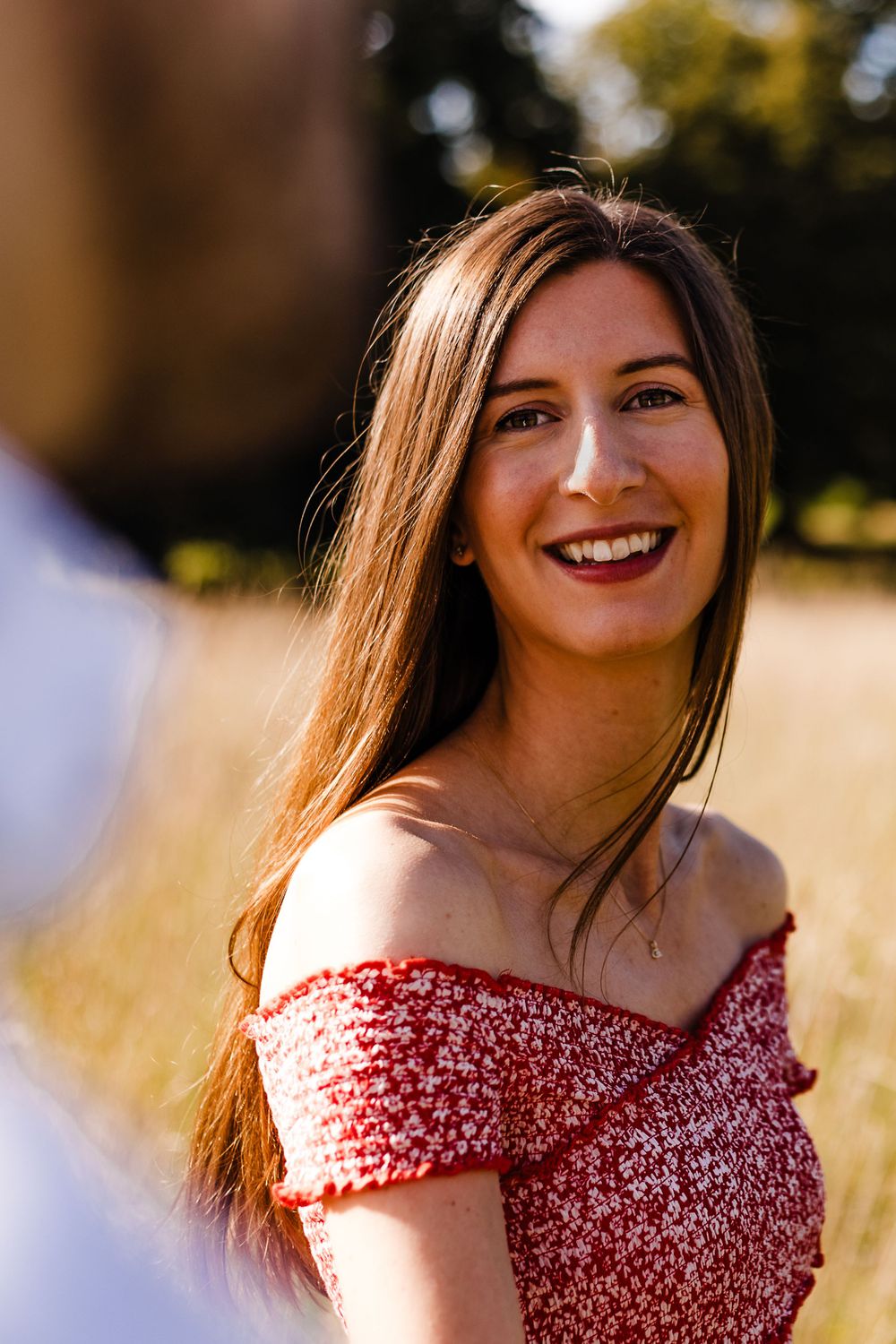 Woman in a red floral dress smiling brightly in golden sunlight.