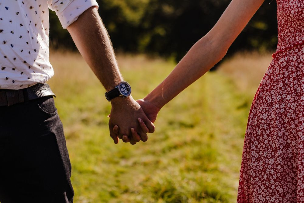 Close-up of couple holding hands outdoors showing casual attire and a watch.