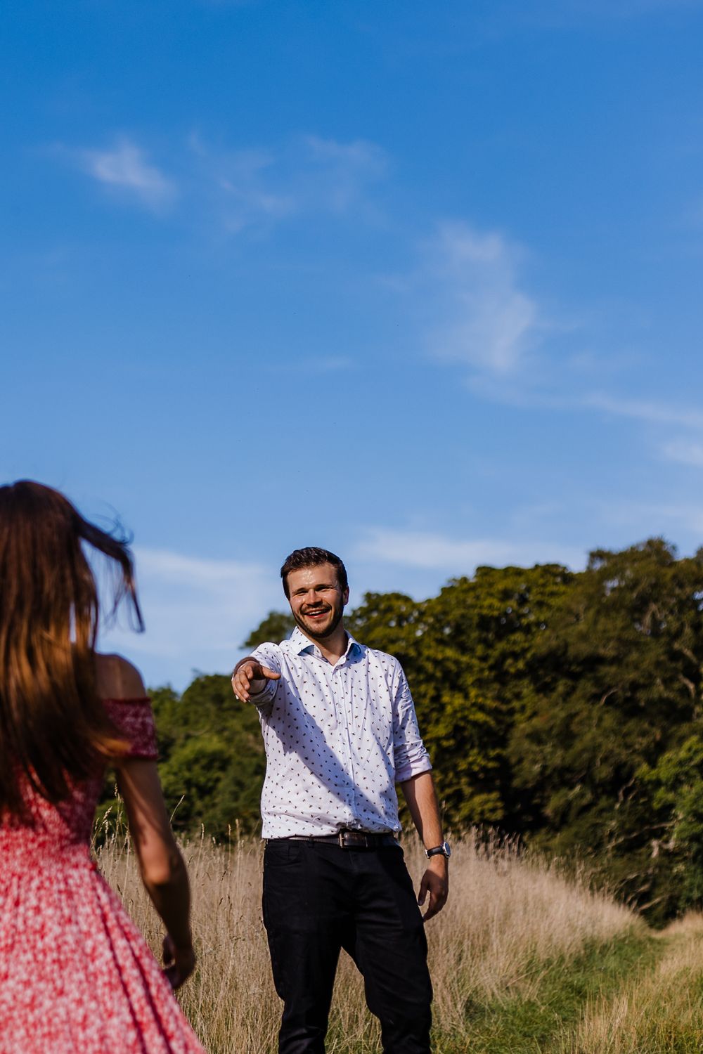 Couple enjoying a sunny day outdoors with trees and tall grass in the background.