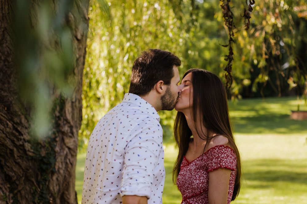 Intimate moment between a couple under a willow tree in a sunlit garden.