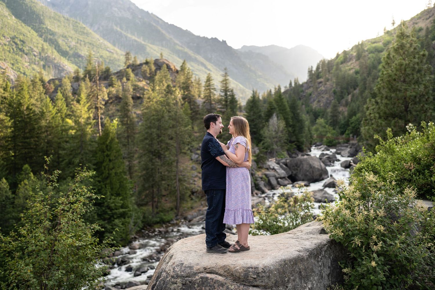 Two people standing on a rocky overlook with mountain vistas and waterfall in background.