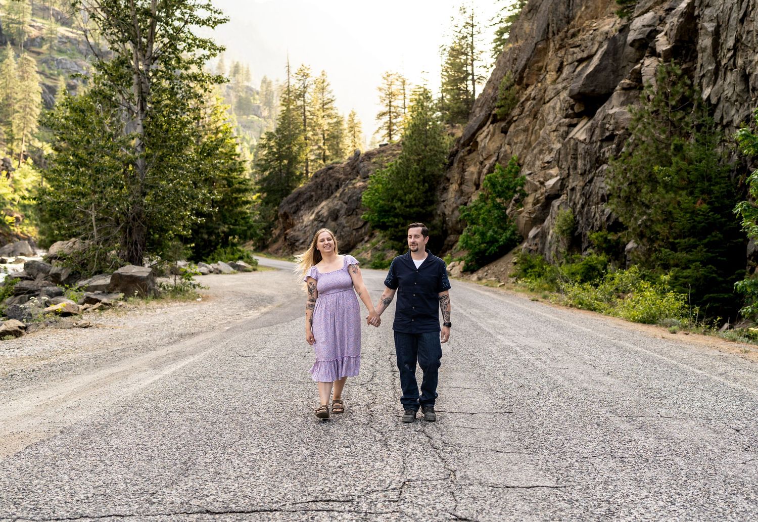 Couple walking hand in hand down a dirt mountain road surrounded by towering cliffs.