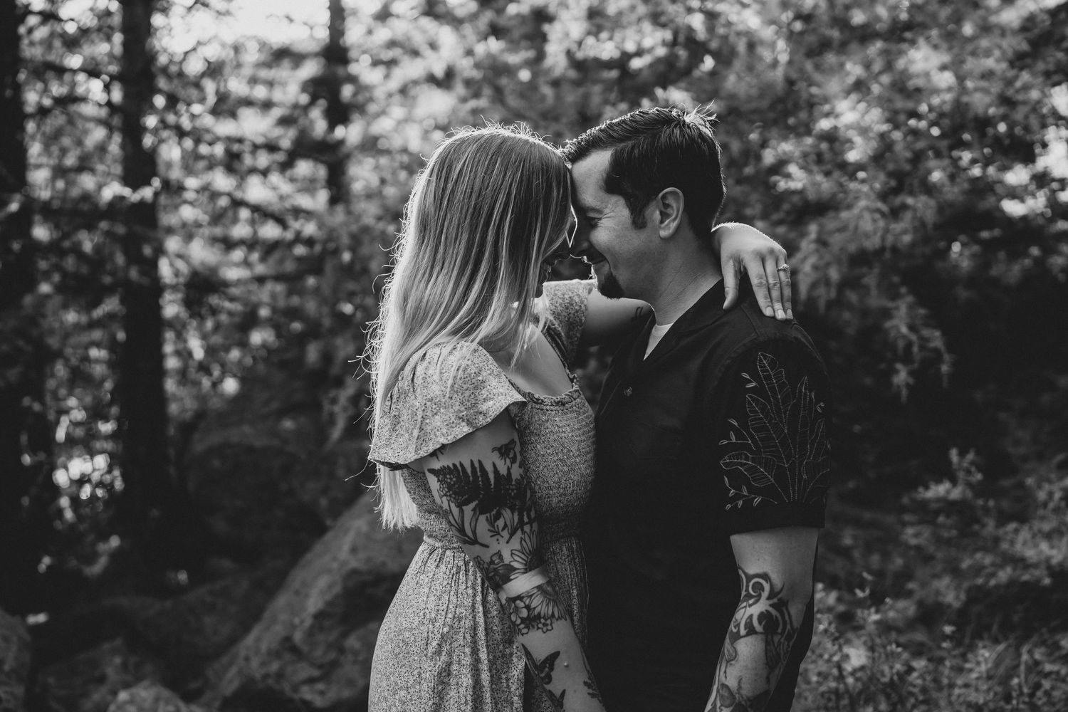 A black and white portrait of an intimate moment between a couple in a wooded setting.