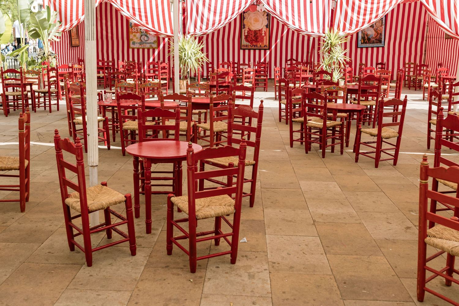 Red wooden chairs and tables arranged under a striped awning in an outdoor dining patio setting in Seville, Spain