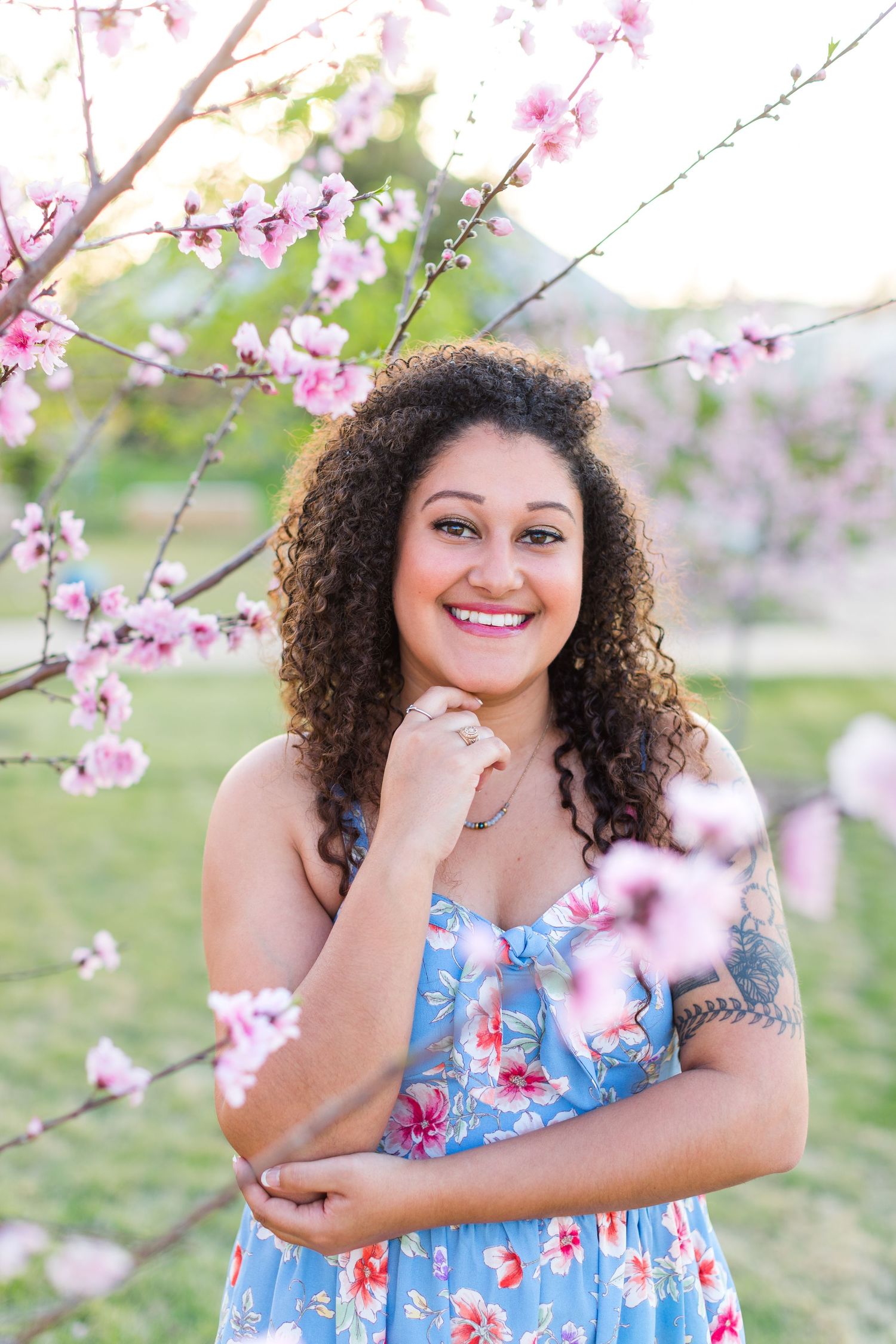 Spring portrait with cherry blossoms framing a floral dress against soft pink blooms.