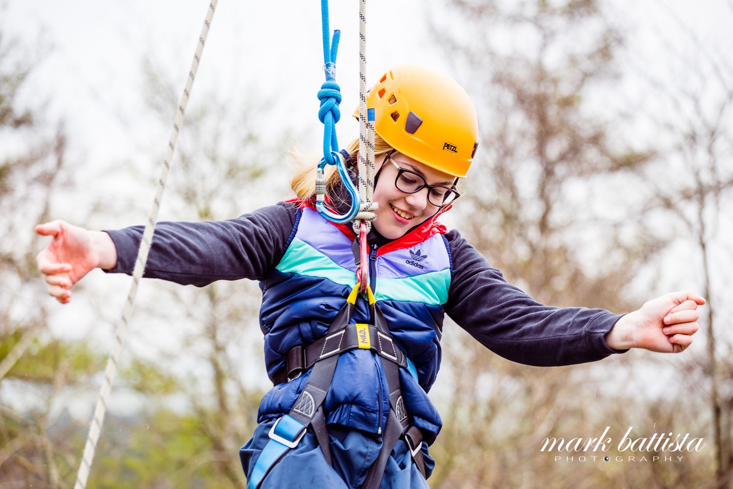 A participant in adaptive sports equipment enjoying a zipline adventure while wearing a yellow helmet.