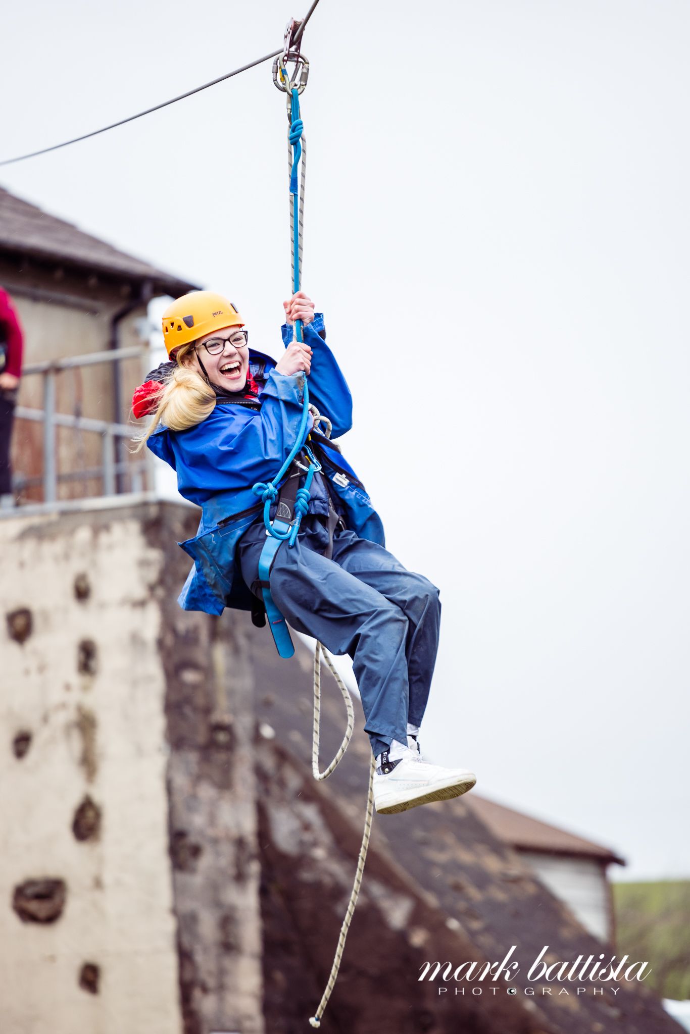 Someone in a blue jacket and yellow helmet enjoying an outdoor zip line activity.