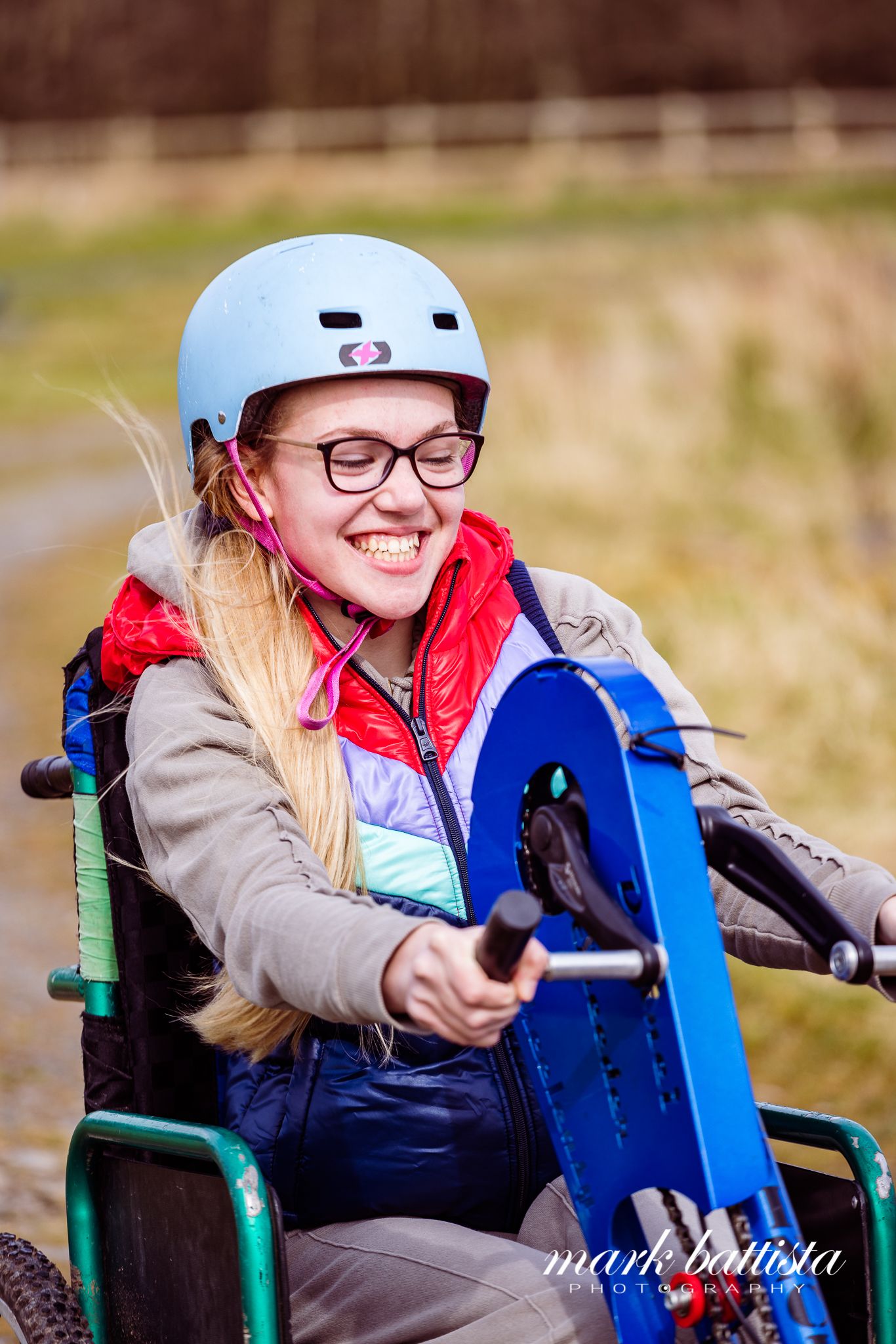 Adaptive athlete in a wheelchair holding a blue wakeboard and wearing safety gear.