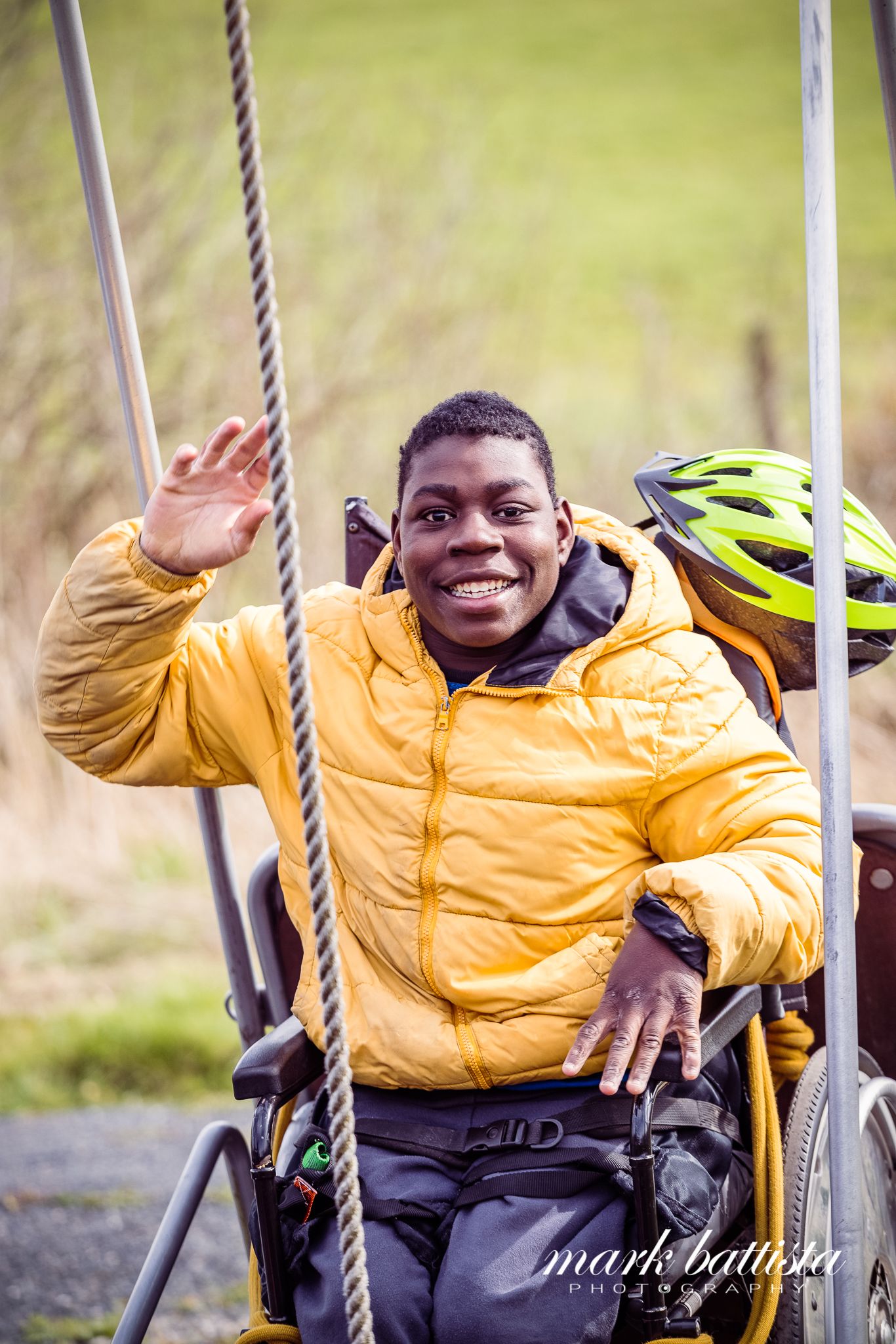 Adaptive athlete in a yellow jacket waving happily from adaptive sports equipment.