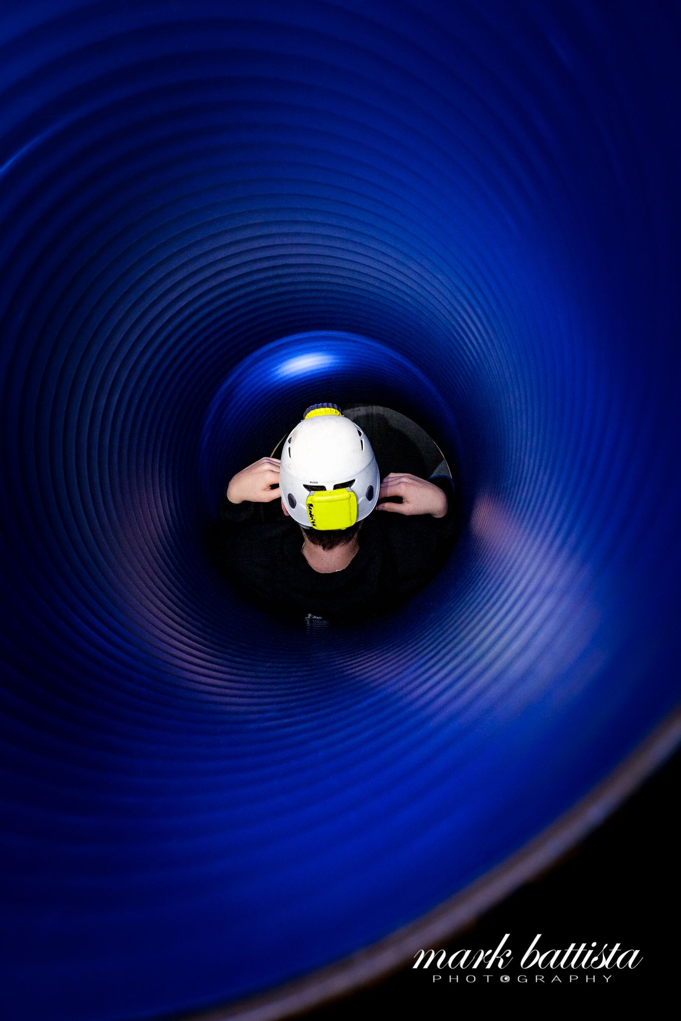 A view looking down through a deep blue spiral tunnel showing someone wearing a white helmet.