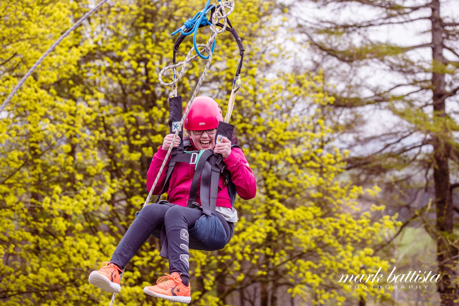Someone in a pink helmet and safety gear zip lining through yellow autumn foliage.
