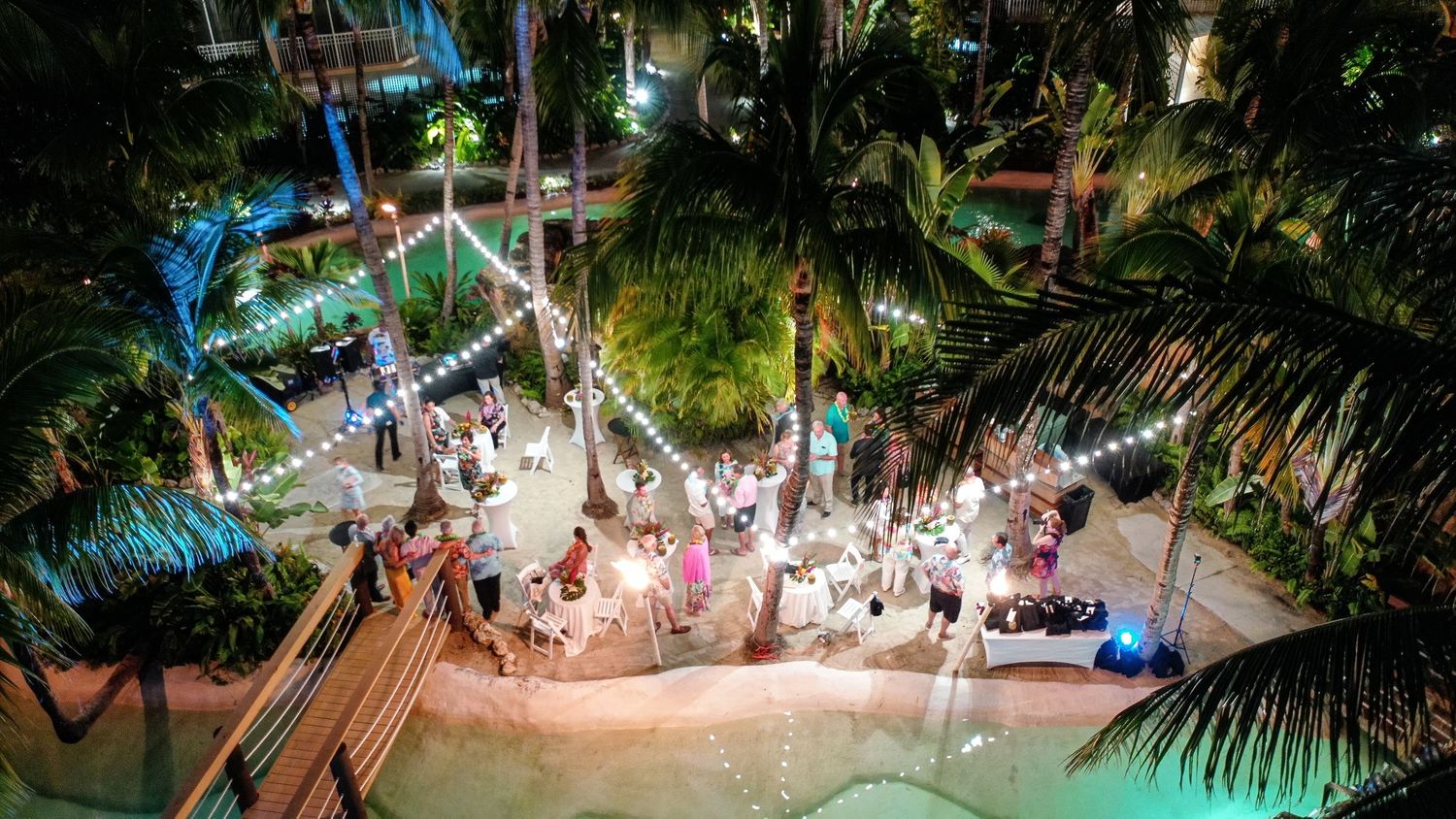 Elegant tropical destination wedding ceremony at sunset under palm trees and cabanas with white fabric draping.