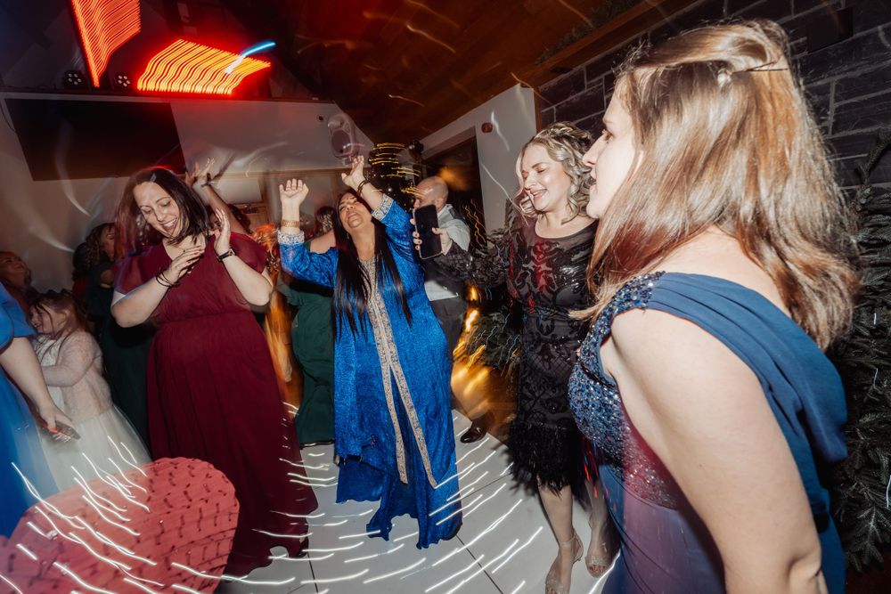 Wedding guests dancing energetically at a reception with dramatic lighting effects.
