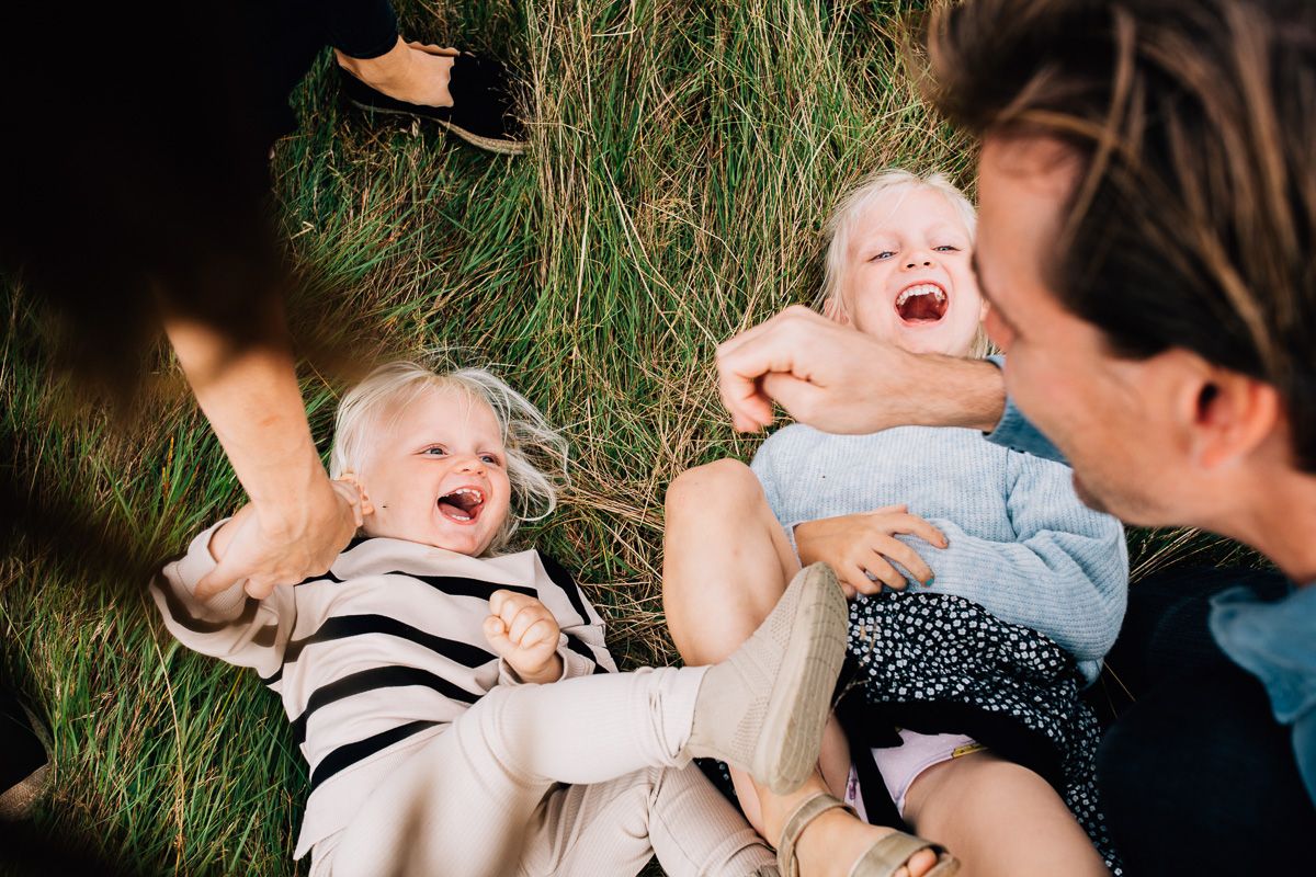 A candid family moment filled with laughter while laying in tall grass.