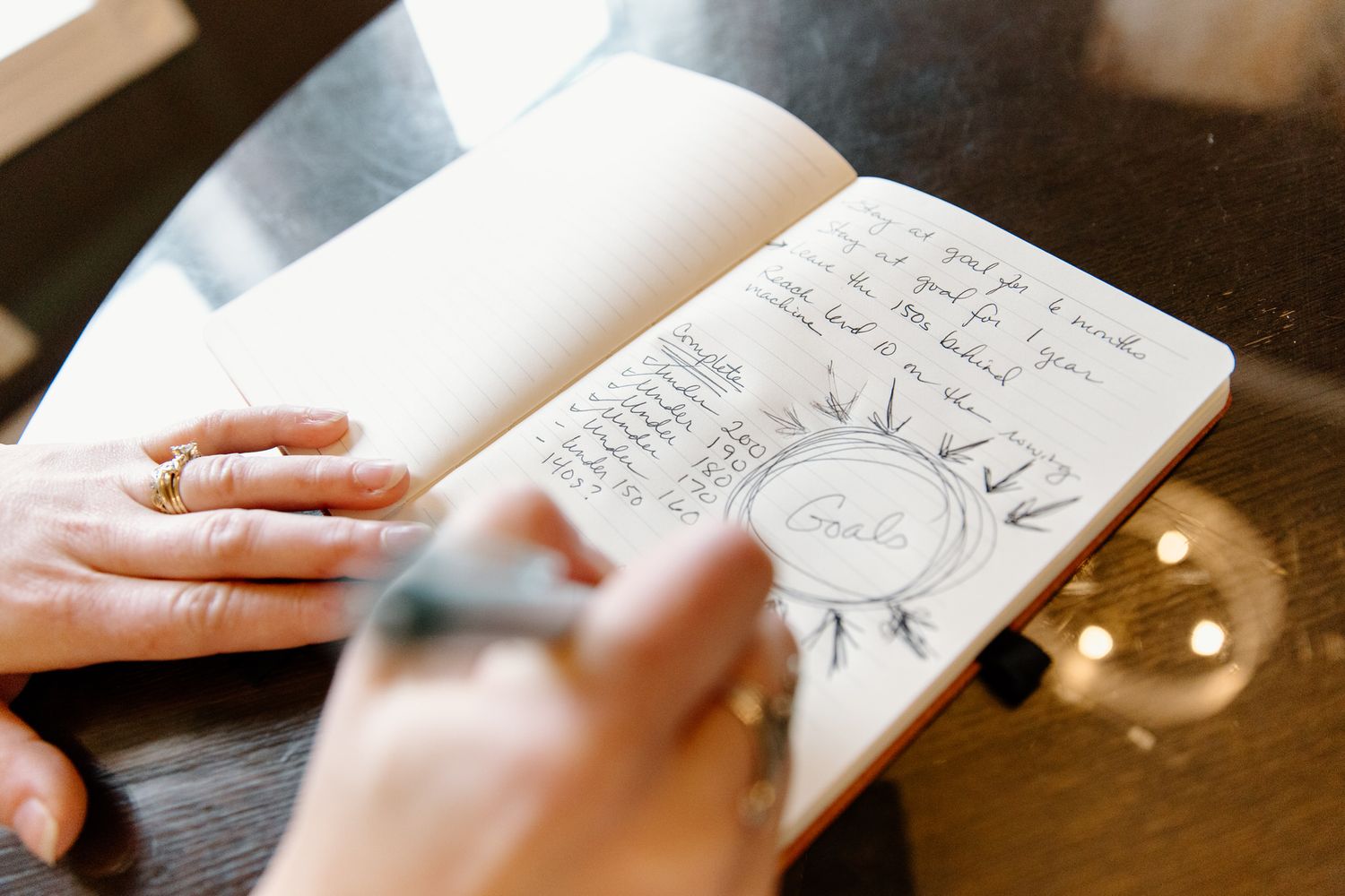 Hands writing and sketching in notebook with warm lighting.