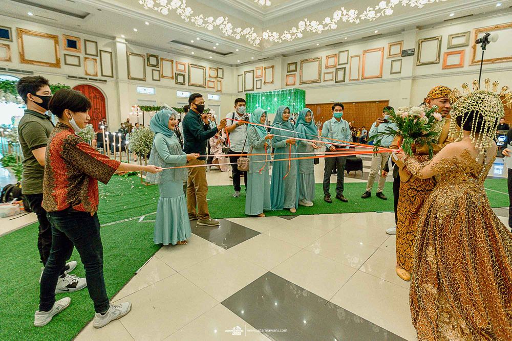 Guests participate in an indoor wedding game with red ribbons on artificial grass.