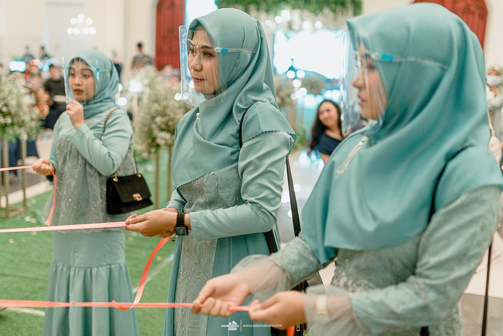 Women in mint green hijabs participate in a wedding activity with ribbons.