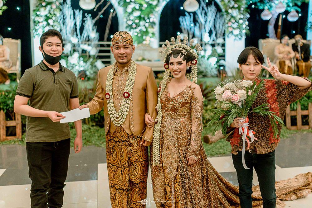Wedding party poses in traditional Indonesian attire with event staff.