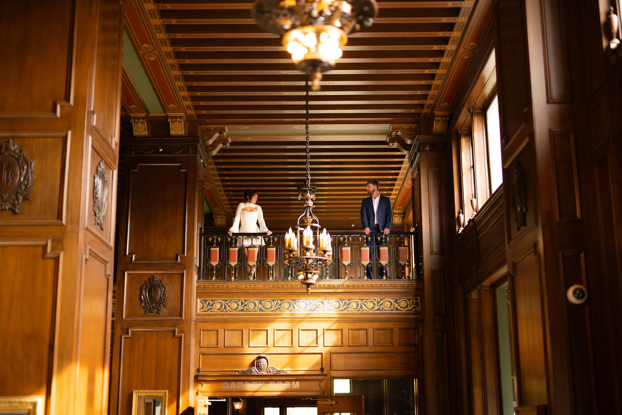 Elegant wooden interior of a grand hall with chandeliers and ornate detailing.