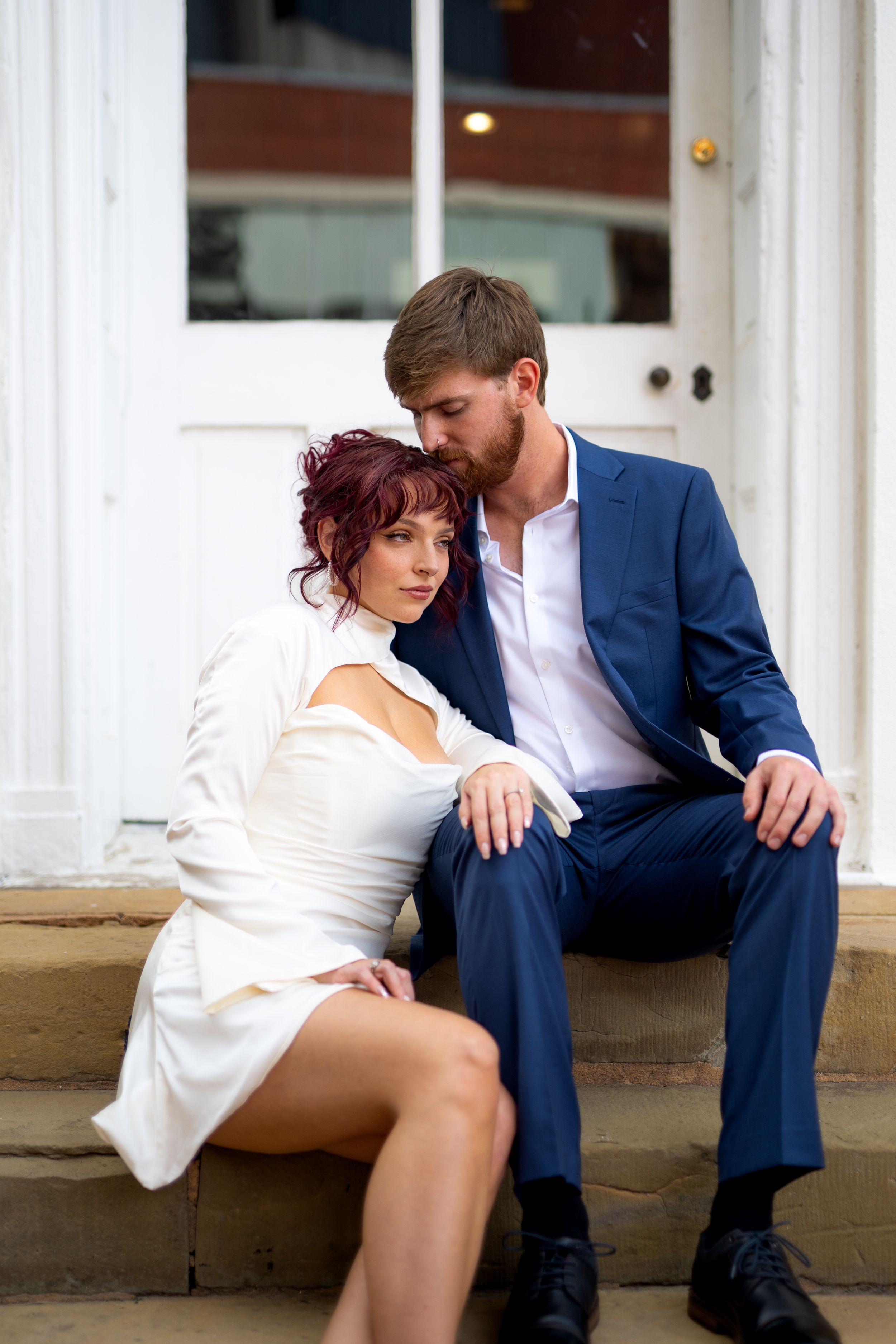 A couple in formal wear shares an intimate moment while sitting on stone steps.
