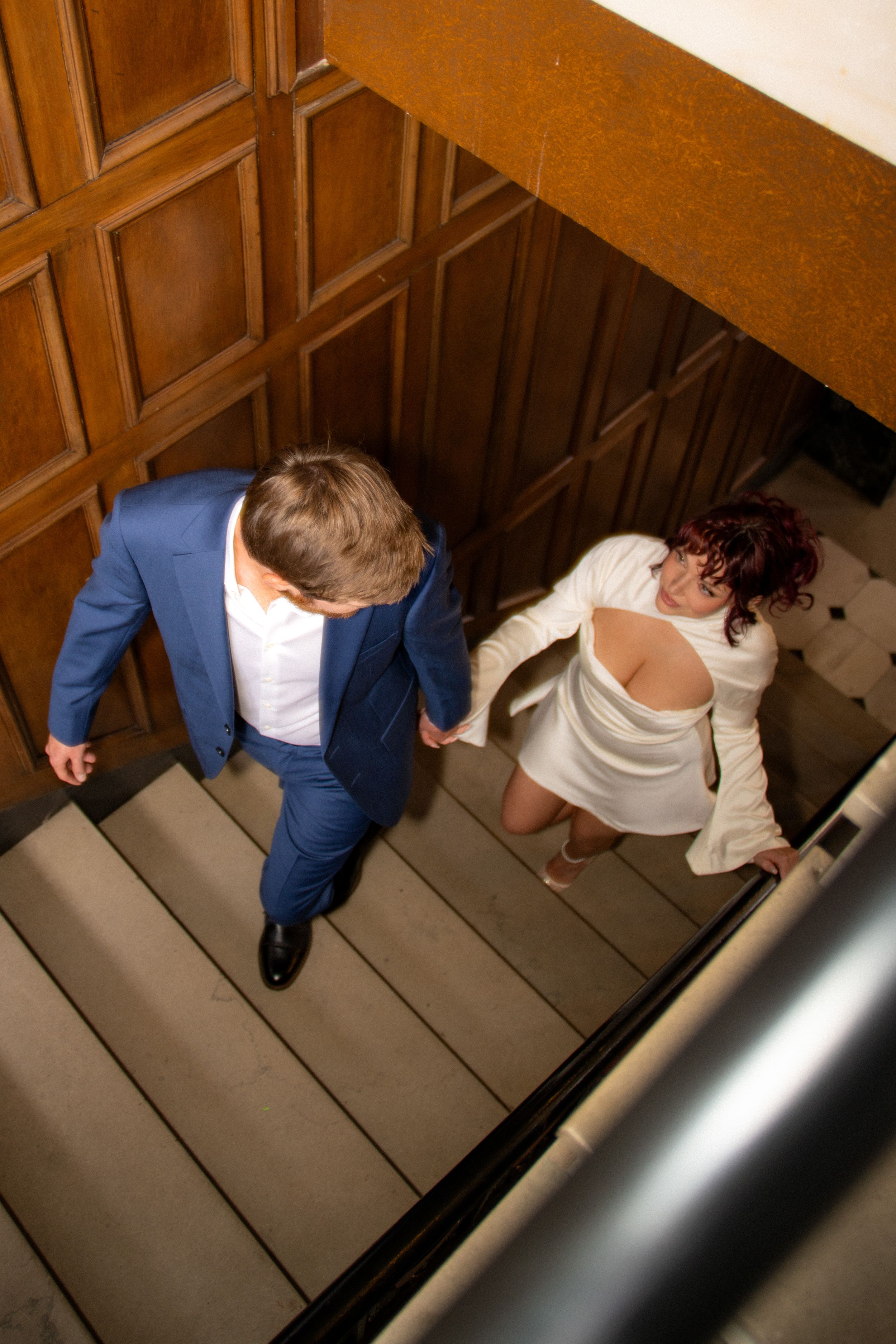Overhead view of couple walking down wooden stairs in formal wedding attire.