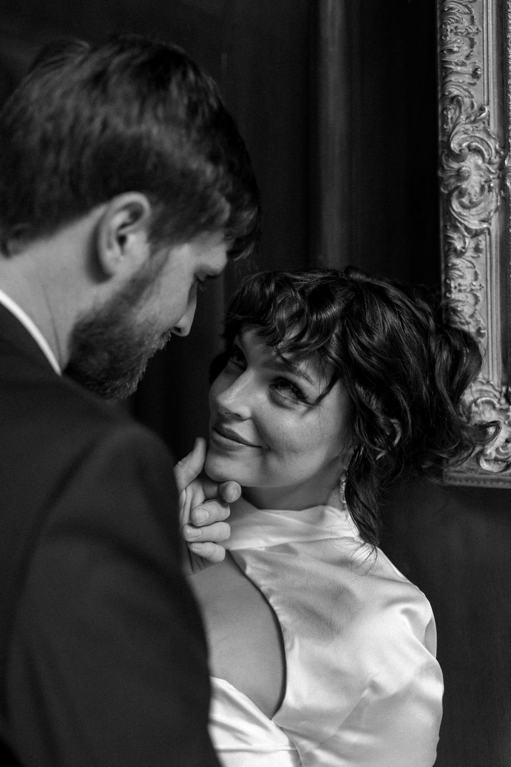 Black and white intimate portrait of a couple with ornate frame in background.
