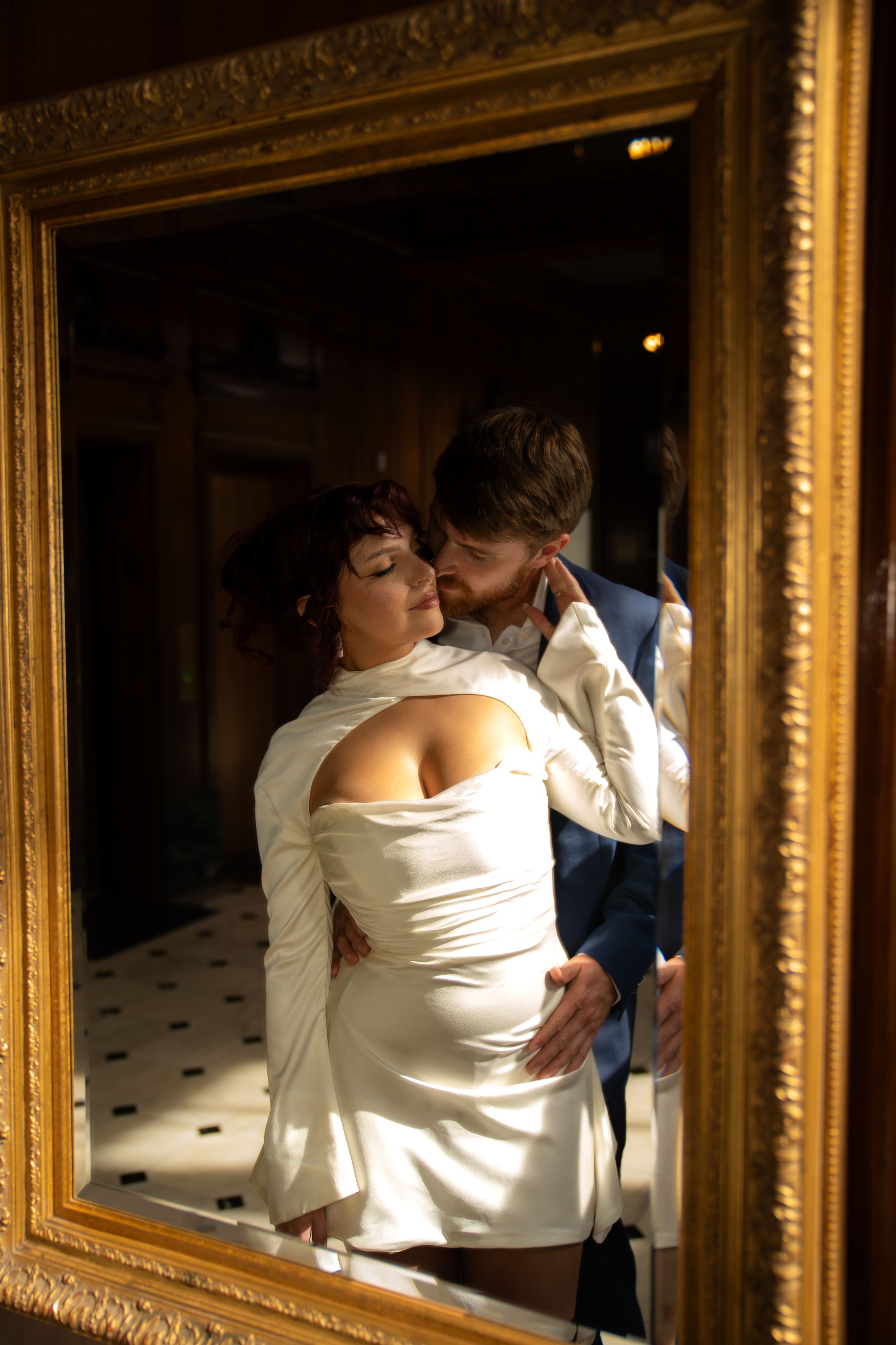 Romantic moment reflected in ornate gold-framed mirrors showing a couple in formal attire.