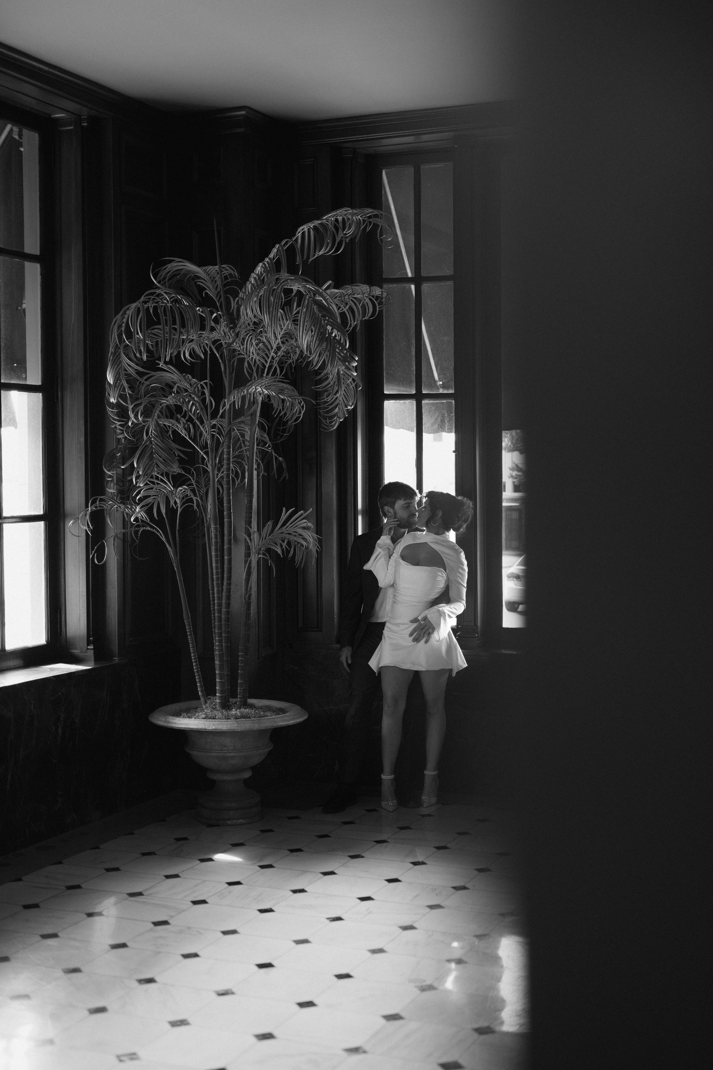 Black and white scene showing silhouettes against bright windows in an elegant room with a tiled floor.